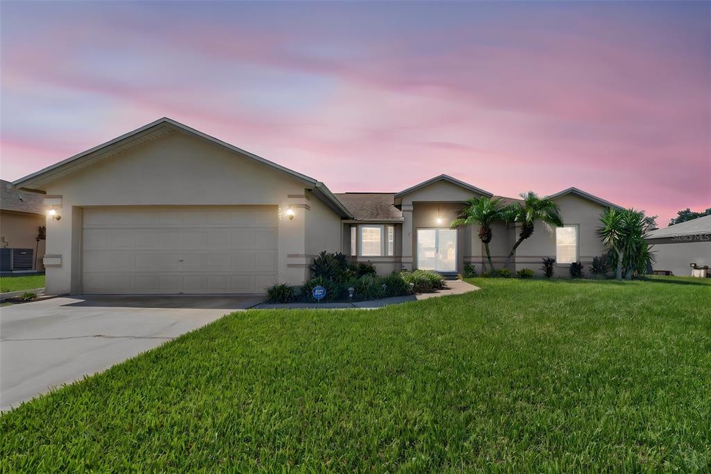 A single-story suburban house with a two-car garage and a front lawn at sunset — 706 HIGHLAND CREST LOOP, LAKE WALES, FL