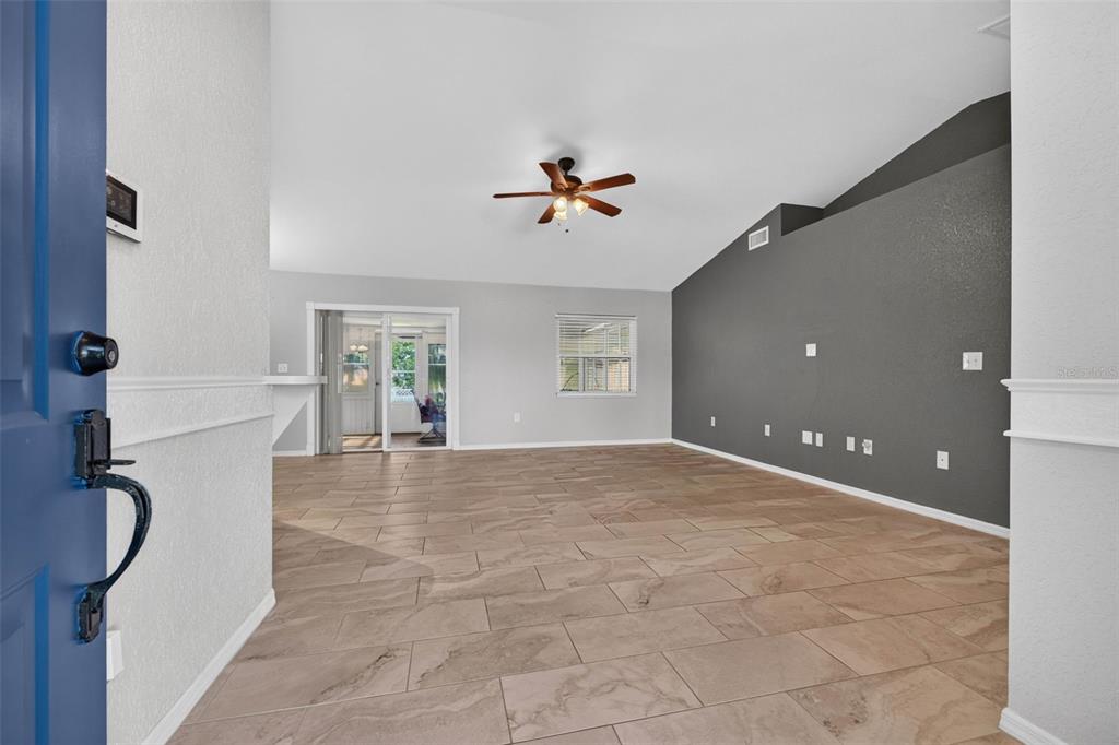 An open living room features light tile flooring, a vaulted ceiling, and a dark accent wall — 706 HIGHLAND CREST LOOP, LAKE WALES, FL