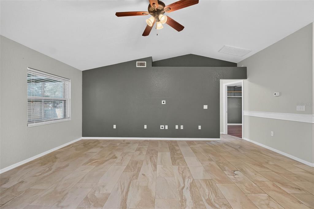 A living room with a vaulted ceiling, a dark gray accent wall, and tiled flooring — 706 HIGHLAND CREST LOOP, LAKE WALES, FL