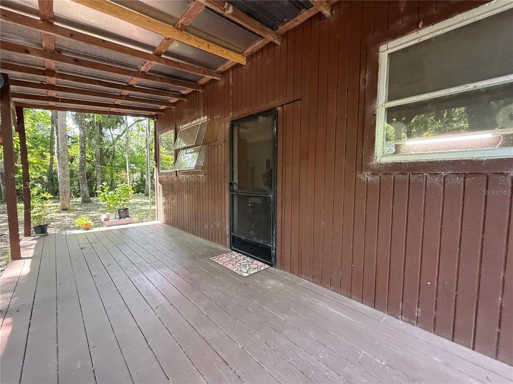 A wooden porch with a screen door, windows, and a corrugated plastic roof — 23946 INDIGO ROAD, ASTOR, FL