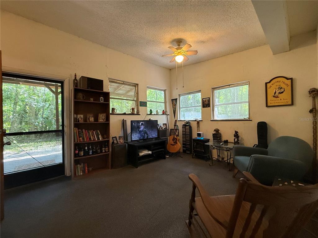 A living room with carpeted floors, a ceiling fan, a bookshelf, and a television — 23946 INDIGO ROAD, ASTOR, FL