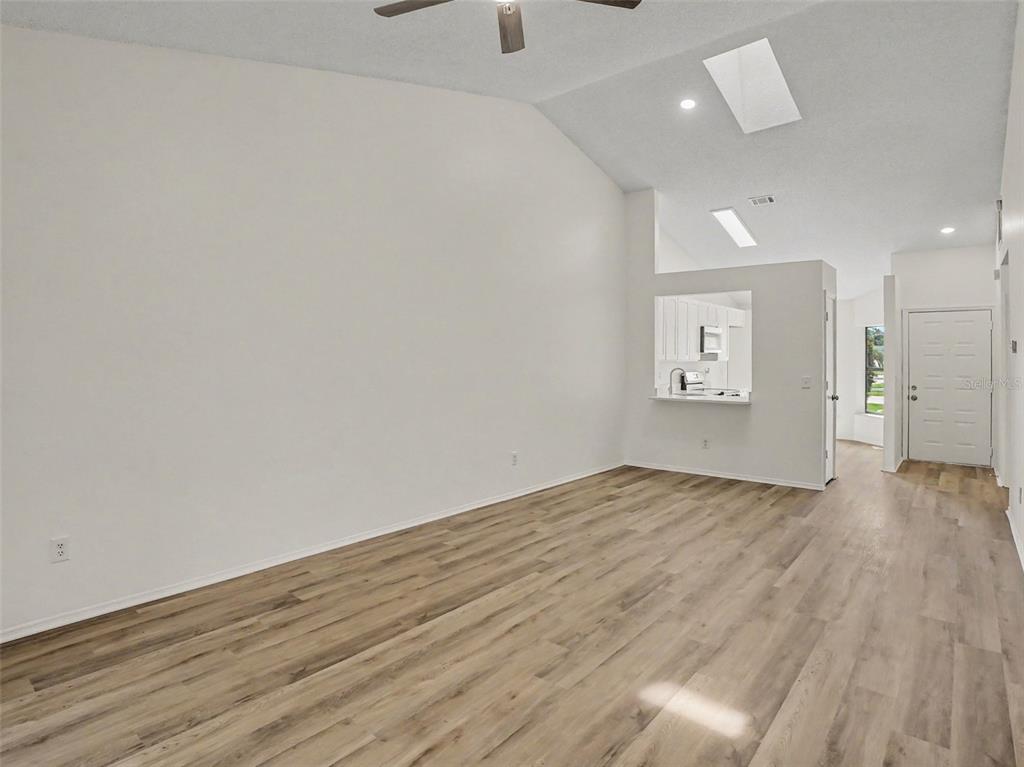 A living room with vaulted ceilings, light wood-look flooring, and an open kitchen pass-through — 84 LAKEPOINTE CIRCLE, KISSIMMEE, FL