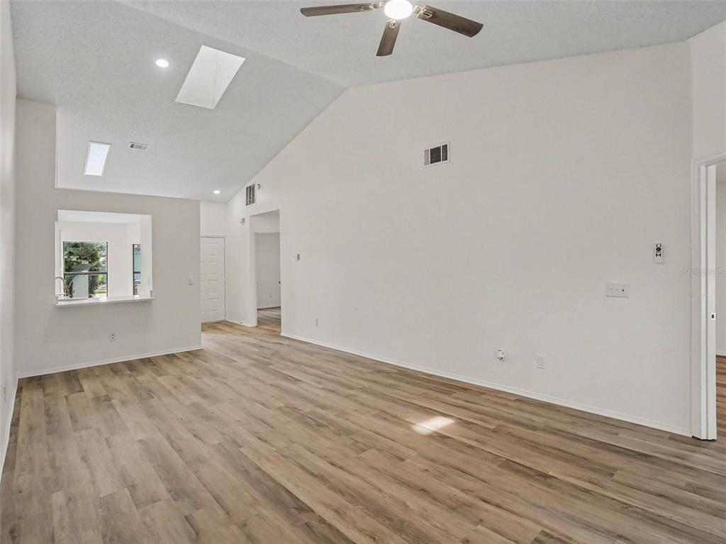 A spacious living room with vaulted ceilings, skylights, wood-look flooring, and a ceiling fan — 84 LAKEPOINTE CIRCLE, KISSIMMEE, FL