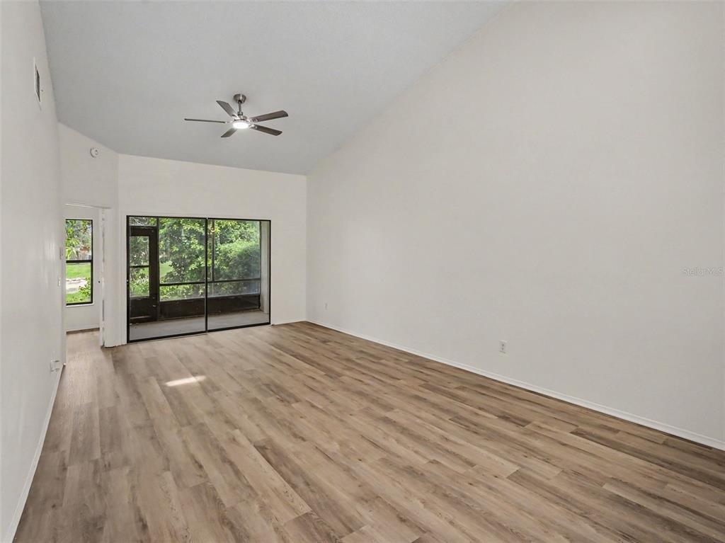 A living room with light wood-look flooring, a vaulted ceiling, a ceiling fan, and sliding doors — 84 LAKEPOINTE CIRCLE, KISSIMMEE, FL
