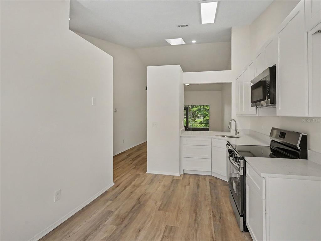 A kitchen with white cabinets, stainless steel appliances, and light wood-look flooring — 84 LAKEPOINTE CIRCLE, KISSIMMEE, FL