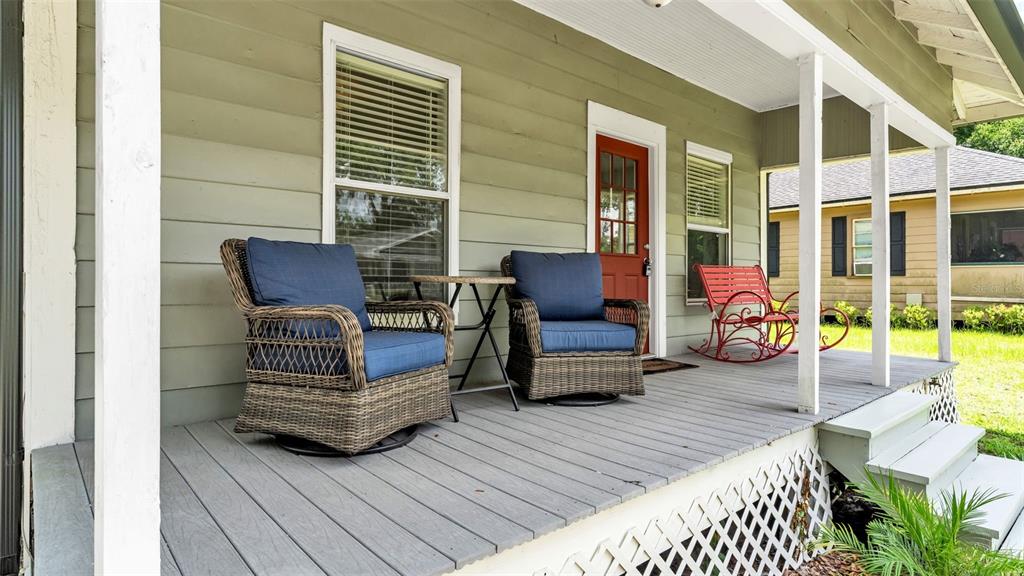 A covered wooden porch features two wicker armchairs, a small table, and a red rocker — 1034 S DAKOTA AVENUE, LAKELAND, FL