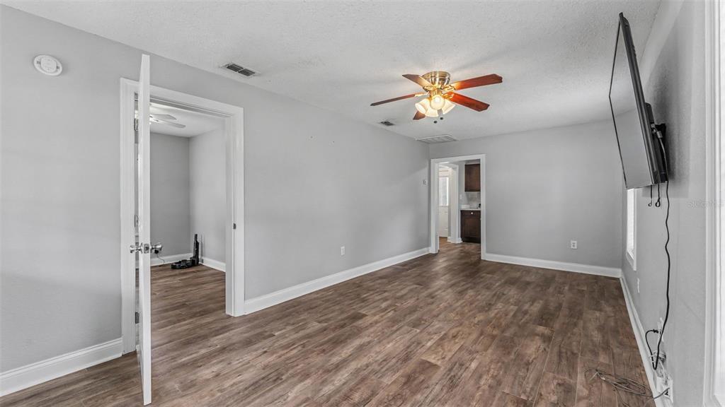 A living room with light gray walls, wood-look flooring, a ceiling fan, and two doorways — 1034 S DAKOTA AVENUE, LAKELAND, FL