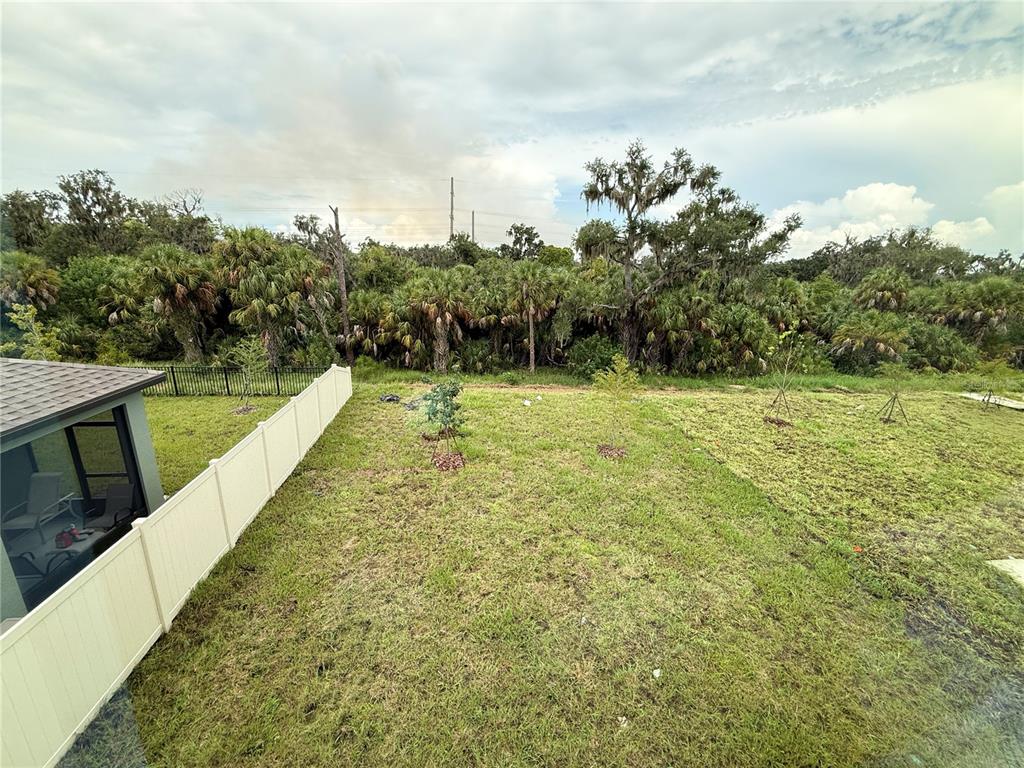 A view of a grassy backyard with a white fence and a wooded area beyond — 10510 CURVING CREEK LOOP, PARRISH, FL