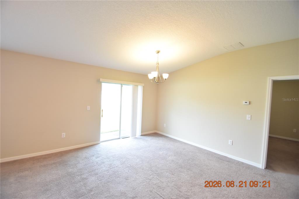 An empty room features beige walls, gray carpeting, a chandelier, and a sliding glass door — 8436 HUNTERS FORK LOOP, RUSKIN, FL