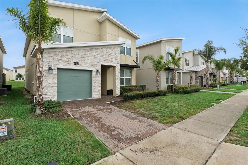 A two-story house with a stone facade, a green garage door, and a brick driveway — 682 WHISTLING STRAITS BOULEVARD, DAVENPORT, FL