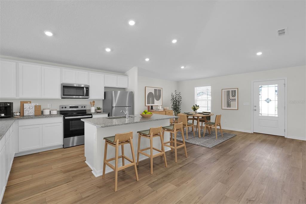 A modern kitchen features white cabinets, granite countertops, stainless steel appliances, and a dining area — 11 PRINCE ANTHONY LANE, PALM COAST, FL