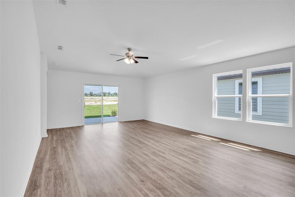 An empty living room features light wood-look flooring, white walls, a ceiling fan, and sliding doors — 11 PRINCE ANTHONY LANE, PALM COAST, FL