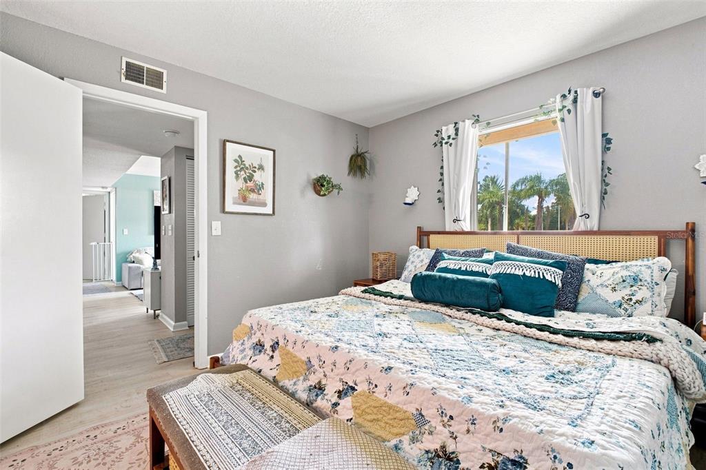 A bedroom features a floral quilt, a rattan headboard, and a doorway leading to another room — 455 ALT 19 S UNIT 17, PALM HARBOR, FL