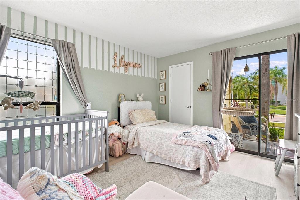 A bedroom features a crib, a twin bed, striped wallpaper, and a sliding glass door — 455 ALT 19 S UNIT 17, PALM HARBOR, FL
