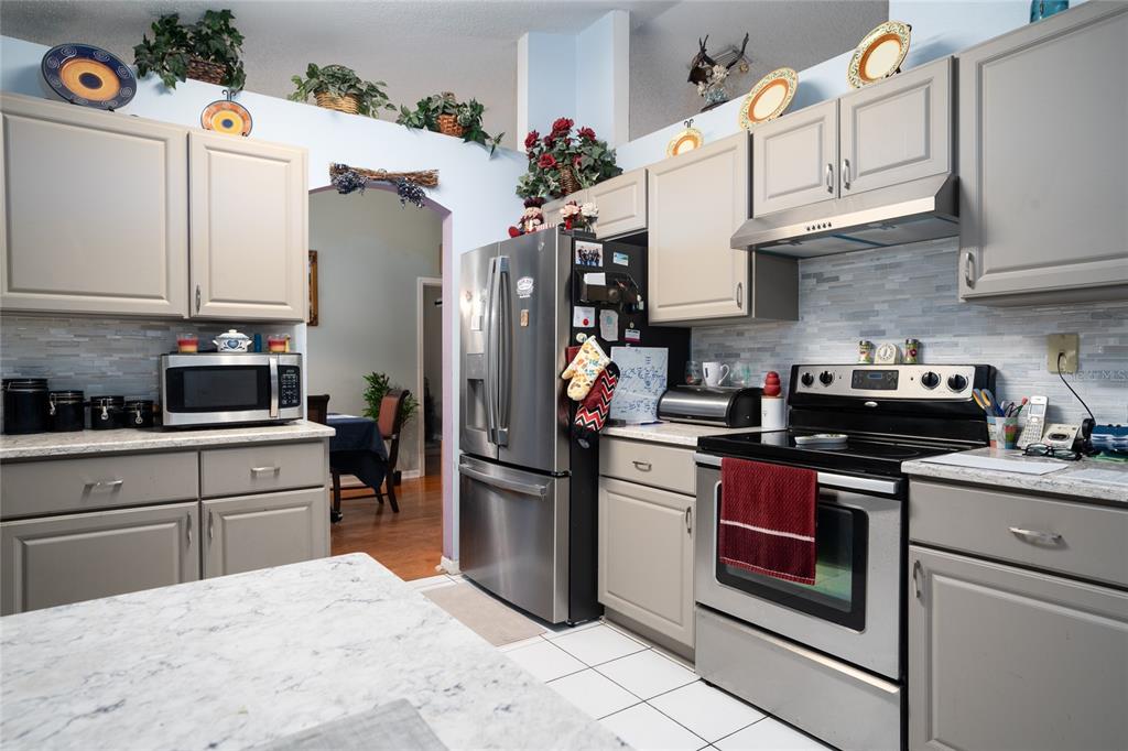 A kitchen features gray cabinets, stainless steel appliances, a marble-look island, and a tiled backsplash — 832 WHITE BIRCH COURT, ORANGE CITY, FL