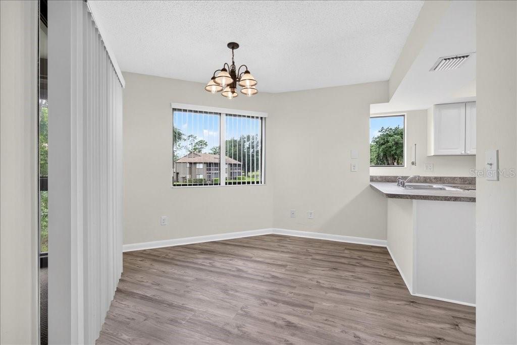 A dining area with wood-look flooring, a chandelier, and a view of an adjacent building — 22 OXFORD LANE UNIT 22, PALM COAST, FL