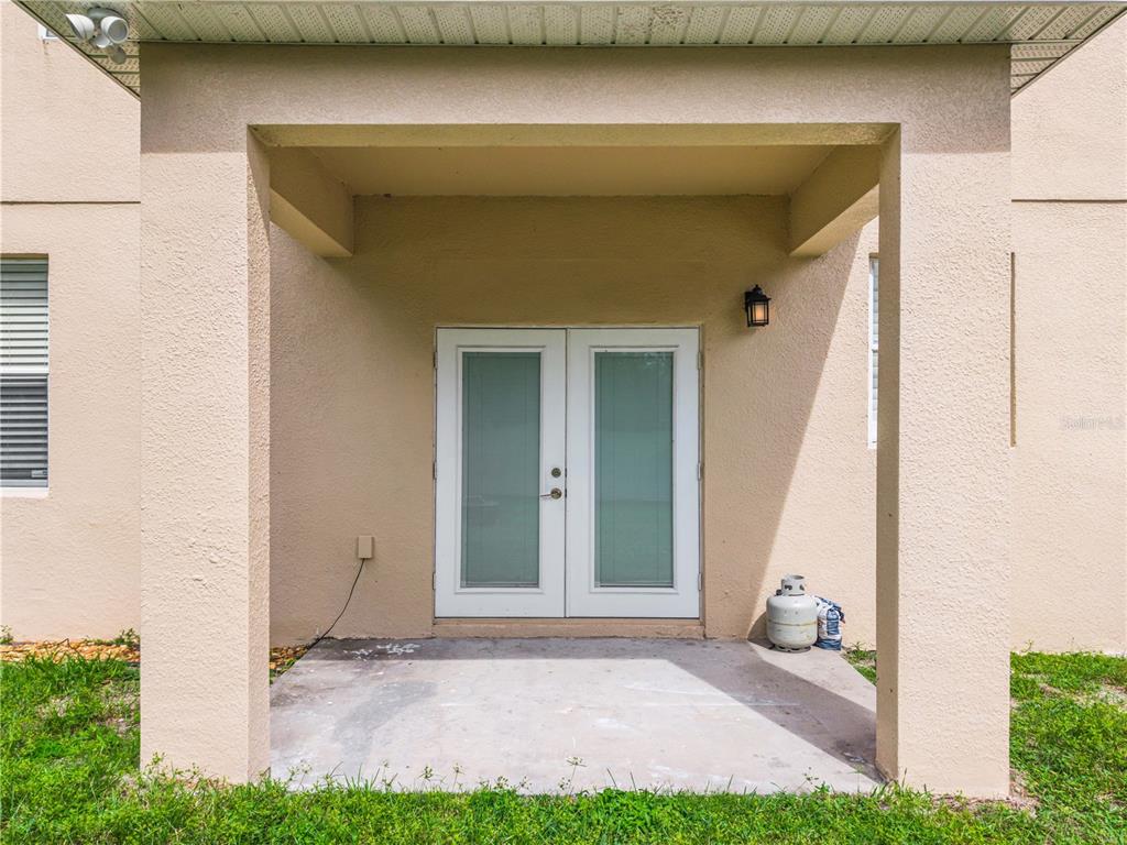 A covered concrete patio features double glass doors and a propane tank against a wall — 3906 QUARTZ AVENUE, ORLANDO, FL
