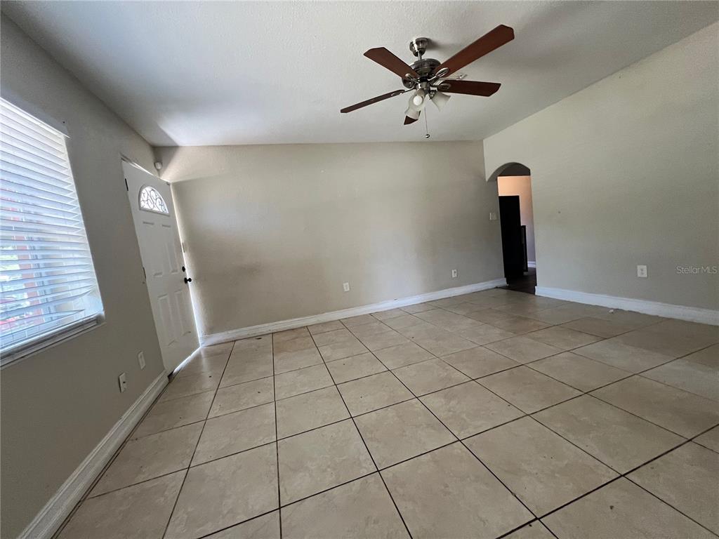 An empty living room features light-colored tile flooring, beige walls, and a ceiling fan — 1011 SANTA BARBARA ROAD, ORLANDO, FL