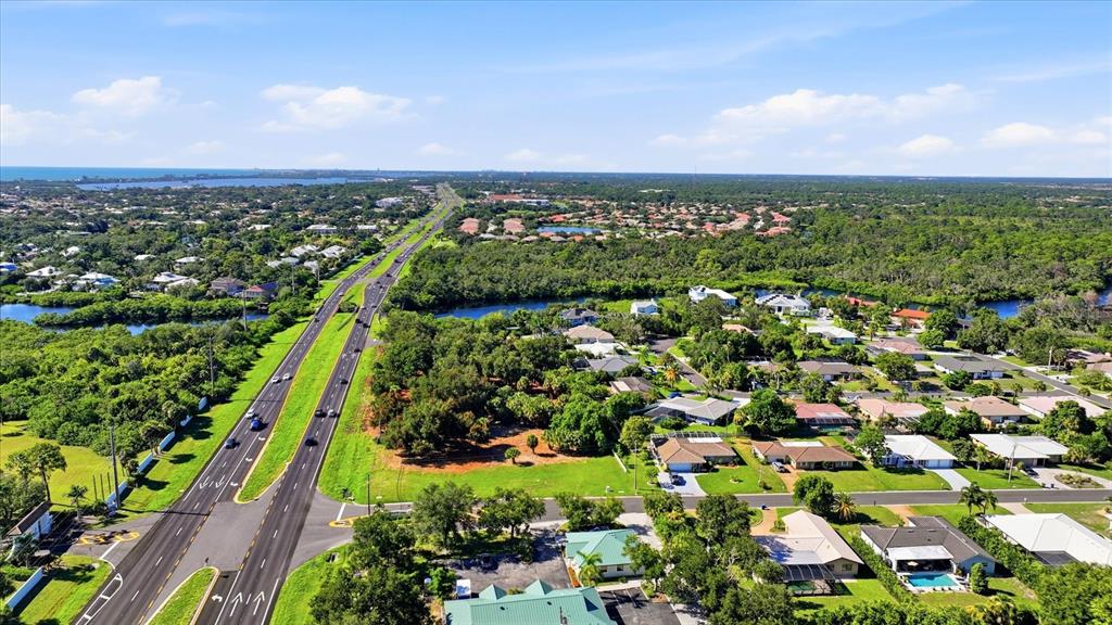 An aerial view shows a coastal neighborhood with houses, mangroves, and a nearby ocean horizon — 2099 S TAMIAMI TRAIL, OSPREY, FL