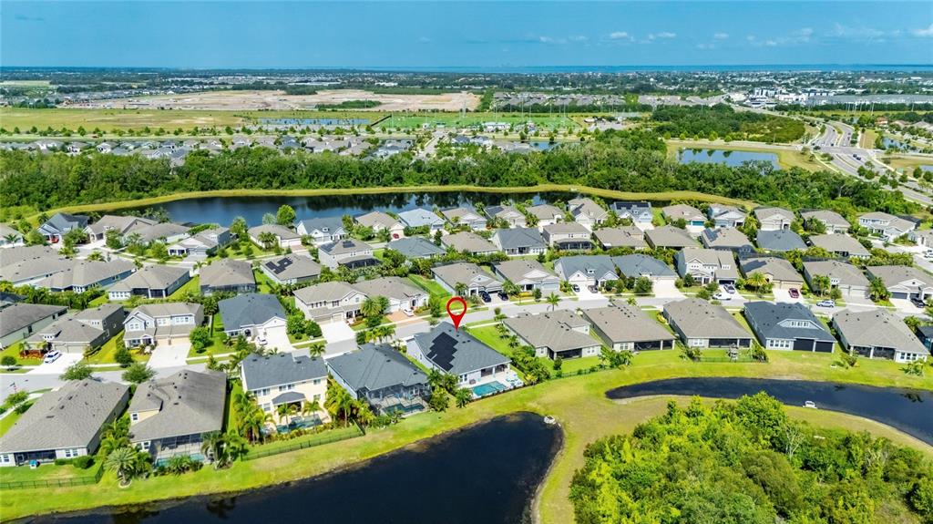 An aerial view shows a suburban neighborhood with houses surrounding a central lake — 7322 PARADISO DRIVE, APOLLO BEACH, FL