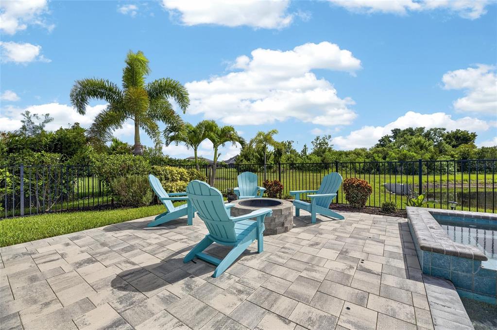 A stone patio features a fire pit, four light blue Adirondack chairs, and a pool — 7322 PARADISO DRIVE, APOLLO BEACH, FL