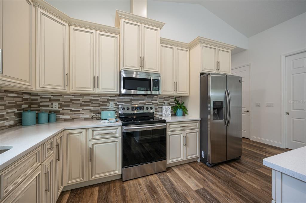 A kitchen features off-white cabinets, stainless steel appliances, a tiled backsplash, and wood-look flooring — 59 GREEN CIRCLE, PALM COAST, FL