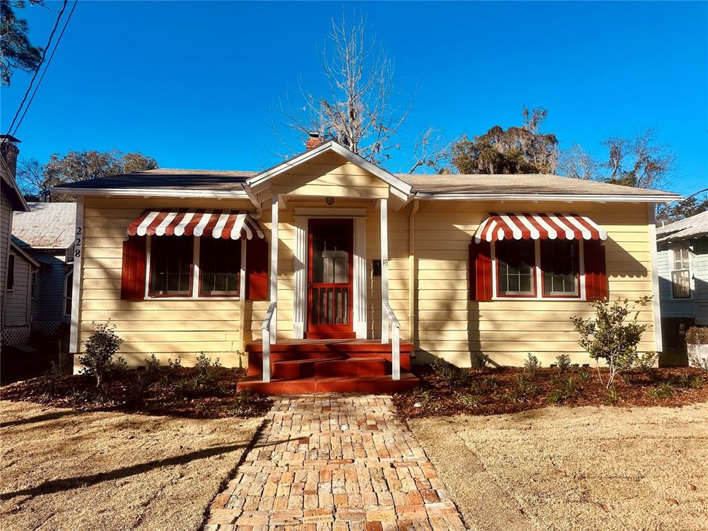 A yellow single-story house features a brick walkway, red shutters, and striped window awnings — 228 NW 4TH AVENUE, GAINESVILLE, FL