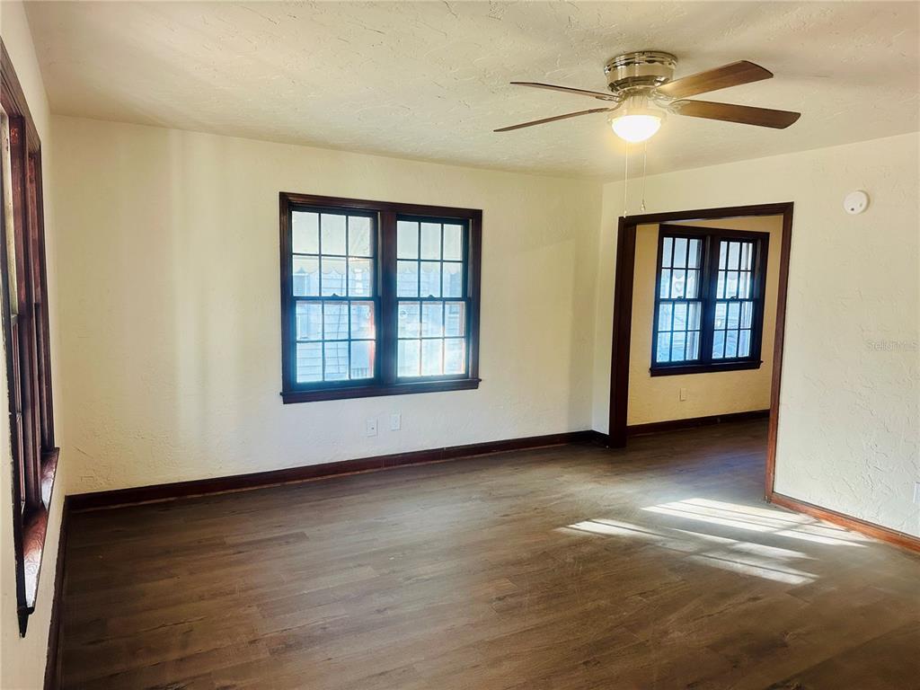 An empty room with wood-look flooring, white walls, dark window trim, and a ceiling fan — 228 NW 4TH AVENUE, GAINESVILLE, FL