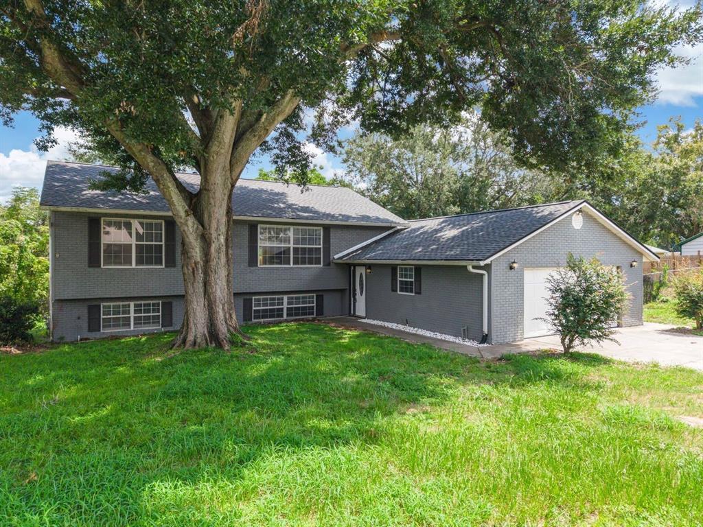 A gray brick split-level house with a large tree in the front yard — 2614 CREST DRIVE, HAINES CITY, FL