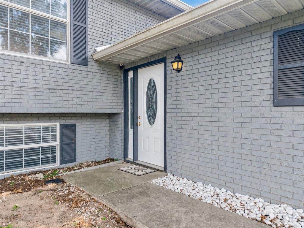 A gray brick house exterior features a white front door with an oval glass insert — 2614 CREST DRIVE, HAINES CITY, FL