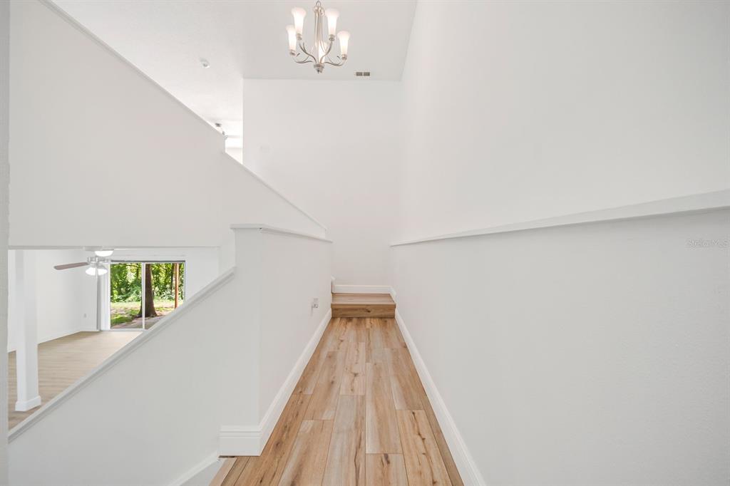 A bright hallway with white walls, wood-look flooring, and a chandelier above the staircase — 2614 CREST DRIVE, HAINES CITY, FL