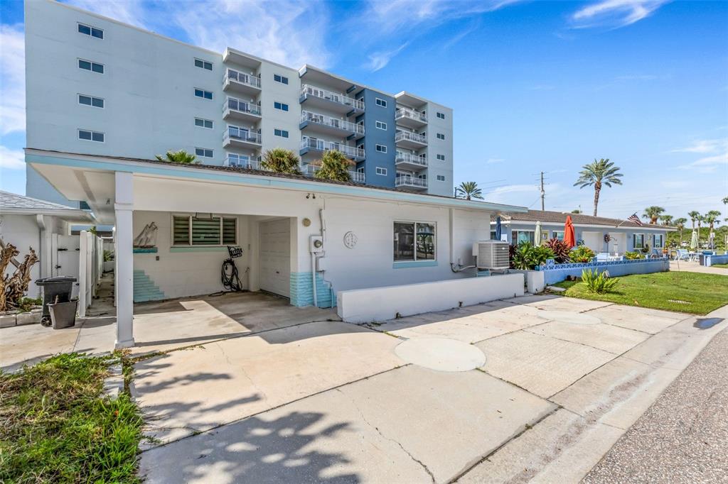 A white single-story house with a carport sits in front of a multi-story apartment building — 18317 SUNSET BOULEVARD, REDINGTON SHORES, FL