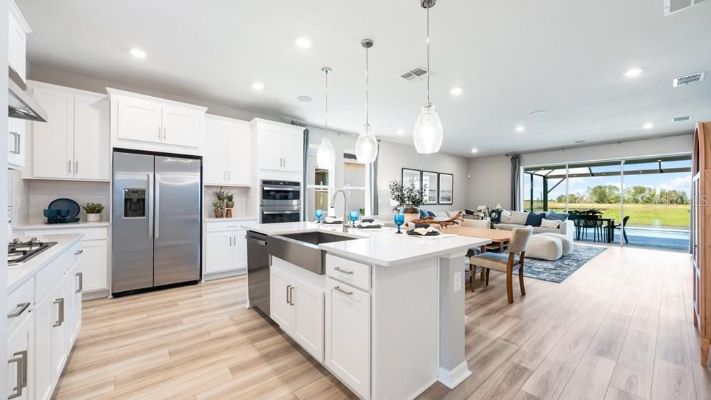 A modern kitchen with white cabinets, stainless steel appliances, and an island overlooks a living area — 5441 GUNWALE DRIVE, COCOA, FL
