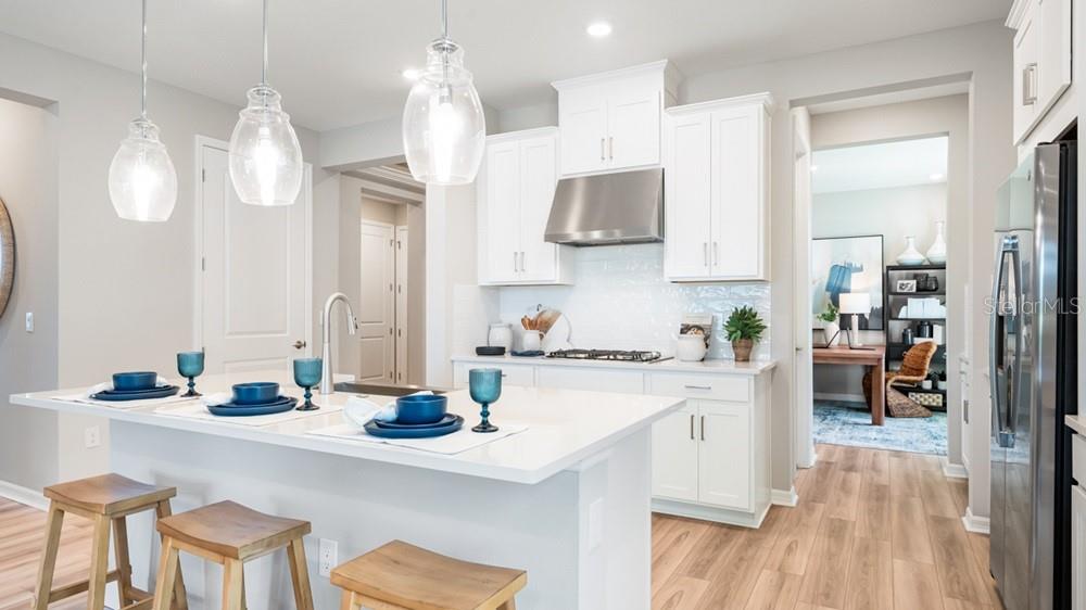 A modern kitchen features white cabinets, stainless steel appliances, a quartz island, and wood flooring — 5441 GUNWALE DRIVE, COCOA, FL