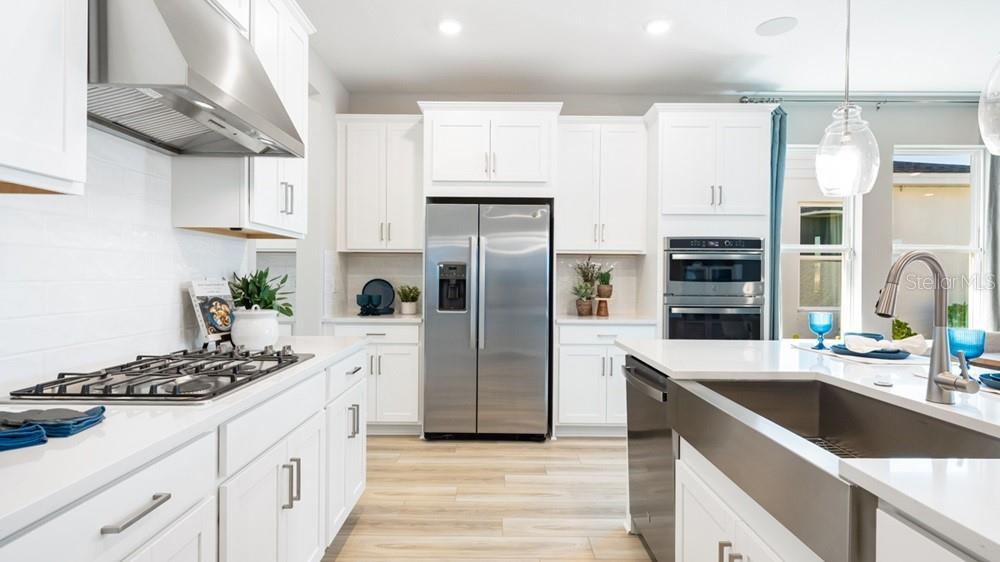A modern white kitchen features stainless steel appliances, a farmhouse sink, and light wood flooring — 5441 GUNWALE DRIVE, COCOA, FL