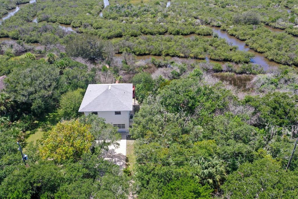 An aerial view shows a house surrounded by dense trees and winding marsh waterways — 1835 OAK PLACE, FLAGLER BEACH, FL