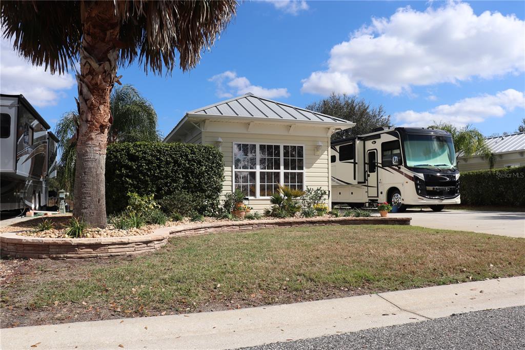 A small, light-colored cottage sits between two large recreational vehicles on a landscaped lot — 9573 SE 49TH TERRACE, WEBSTER, FL