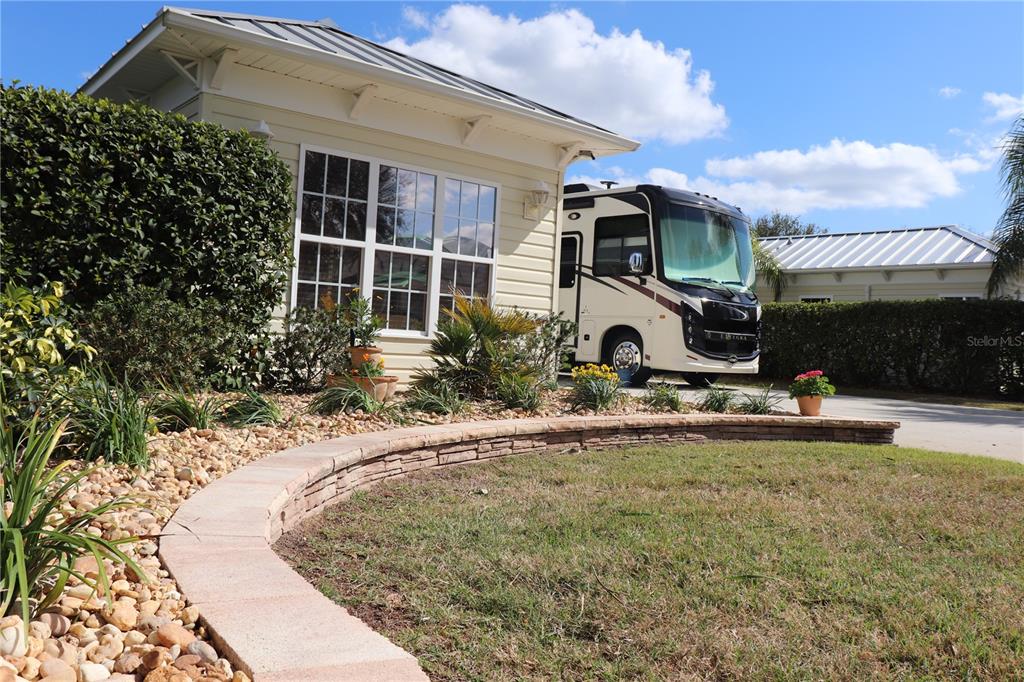 A large recreational vehicle is parked next to a house with a curved stone garden wall — 9573 SE 49TH TERRACE, WEBSTER, FL