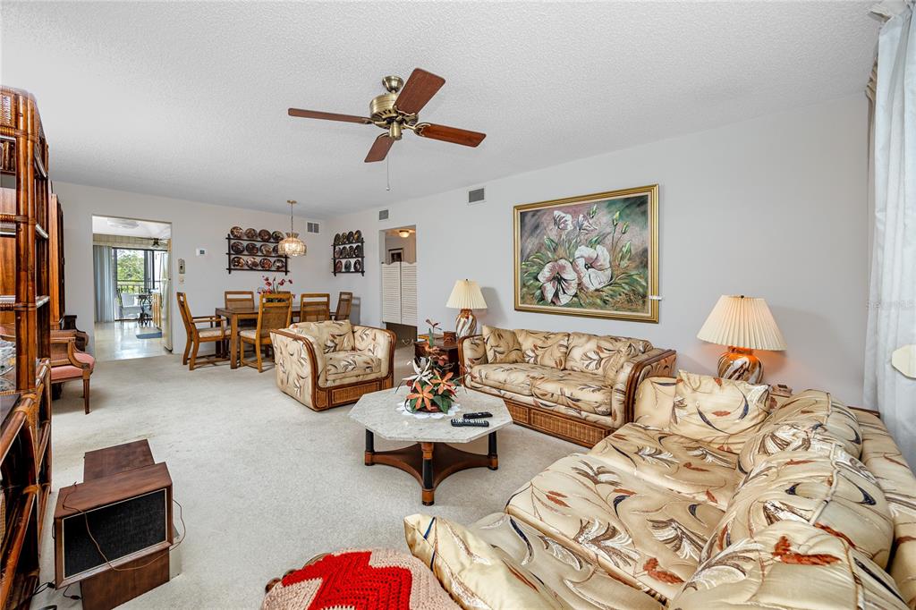 A living and dining room with tropical-patterned furniture, beige carpeting, and a ceiling fan — 8174 TERRACE GARDEN DRIVE N UNIT 307, ST PETERSBURG, FL
