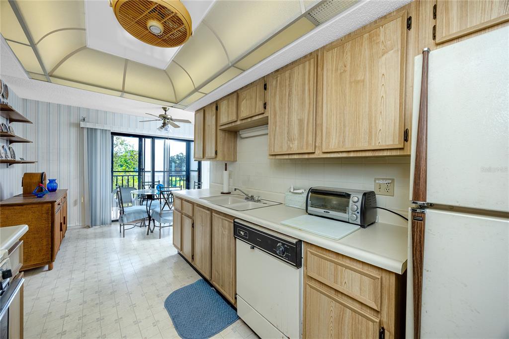 A kitchen with light wood cabinets, white appliances, and a dining area with sliding doors — 8174 TERRACE GARDEN DRIVE N UNIT 307, ST PETERSBURG, FL