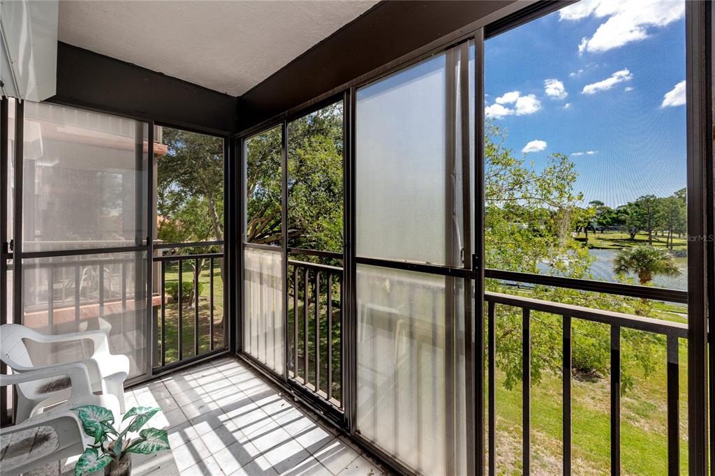 A screened-in balcony with white tile flooring overlooks a grassy area and a small lake — 8174 TERRACE GARDEN DRIVE N UNIT 307, ST PETERSBURG, FL