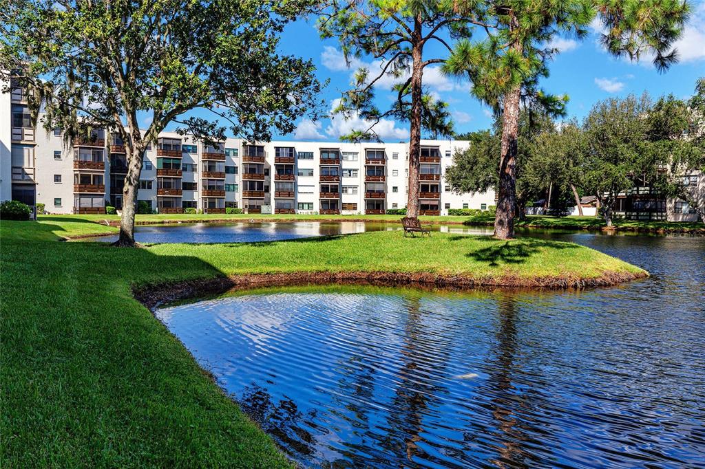 A multi-story apartment building sits behind a grassy lawn and a small pond — 8174 TERRACE GARDEN DRIVE N UNIT 307, ST PETERSBURG, FL