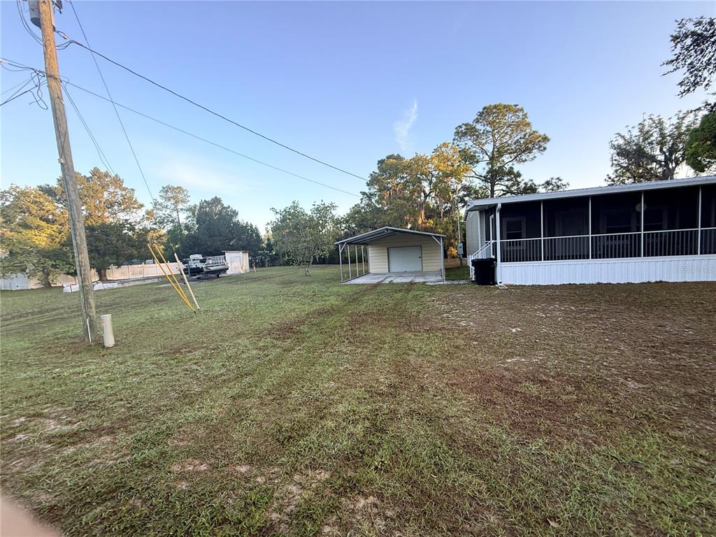 A grassy yard features a detached metal carport and a mobile home with a screened porch — 21809 SUNSET DRIVE, ASTOR, FL