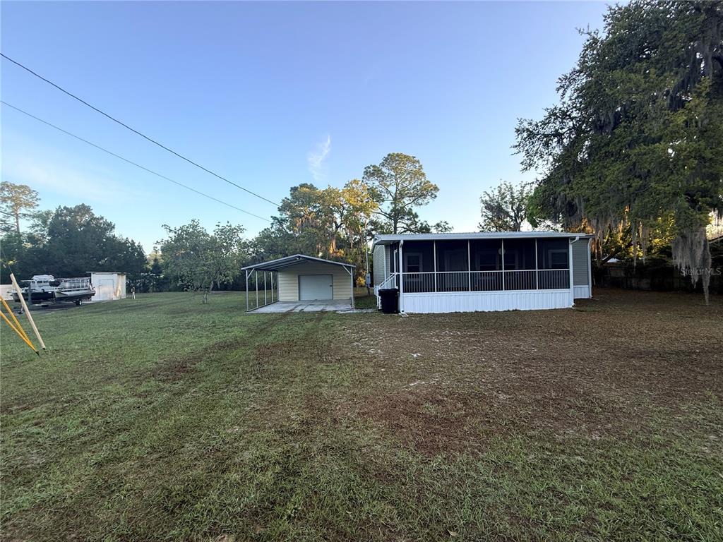 A mobile home with a screened porch and a detached carport on a grassy lot — 21809 SUNSET DRIVE, ASTOR, FL