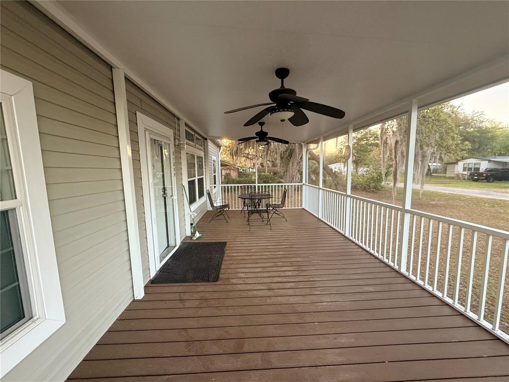 A covered wooden deck features white railings, two ceiling fans, and outdoor furniture — 21809 SUNSET DRIVE, ASTOR, FL