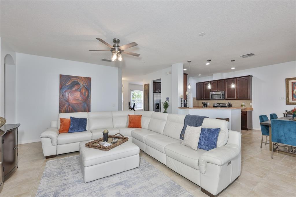 A living room with a white sectional sofa, ottoman, and an open kitchen with dark cabinets — 823 SEMINOLE SKY DRIVE, RUSKIN, FL