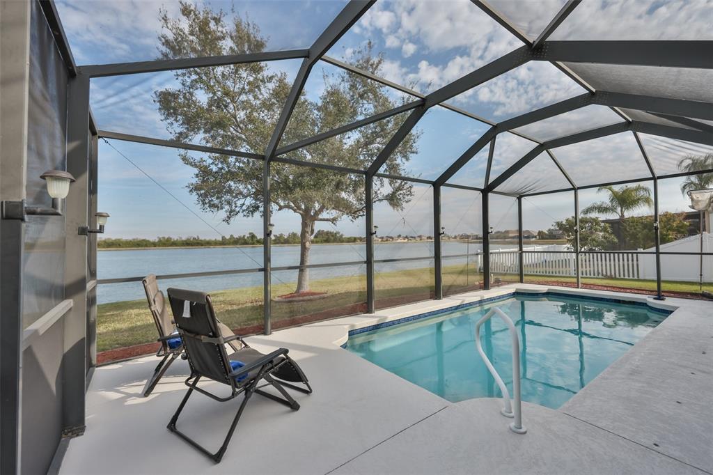 A screened-in pool patio features two lounge chairs overlooking a lake and a white fence — 823 SEMINOLE SKY DRIVE, RUSKIN, FL