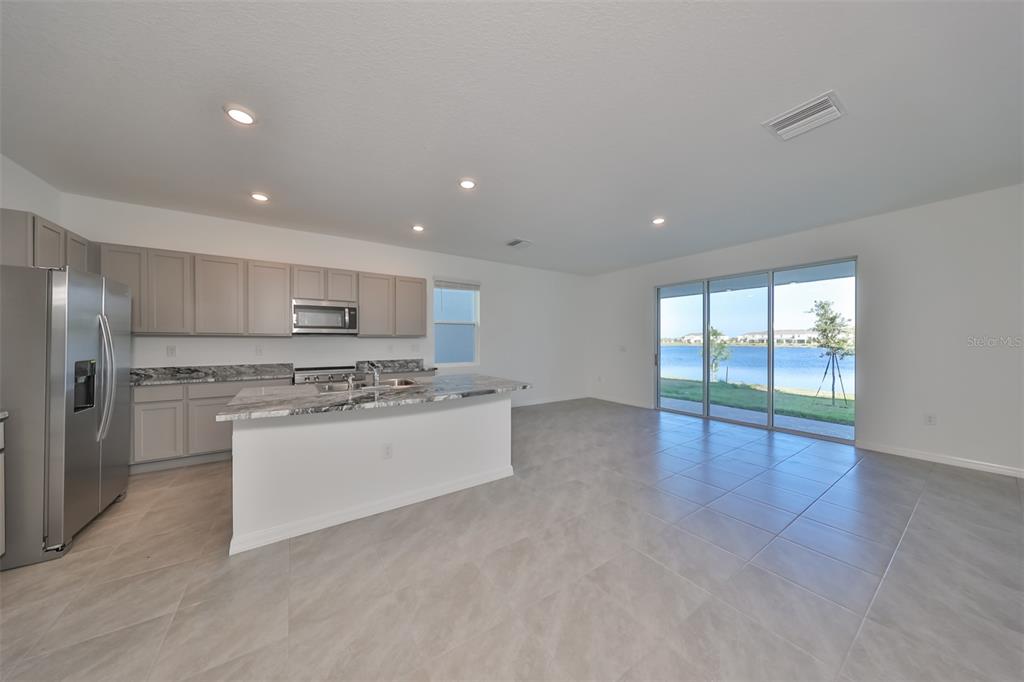 A modern kitchen with gray cabinets and granite countertops opens to a living area with water views — 379 MANGROVE SHADE CIRCLE, APOLLO BEACH, FL