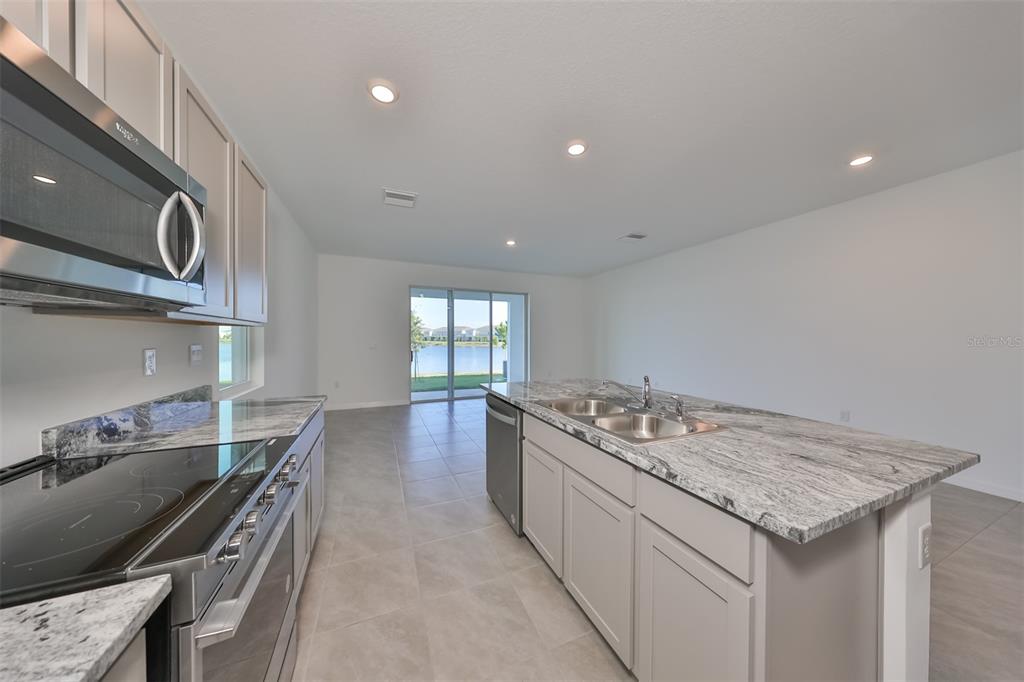 A modern kitchen features light gray cabinets, granite countertops, and a view of a lake — 379 MANGROVE SHADE CIRCLE, APOLLO BEACH, FL