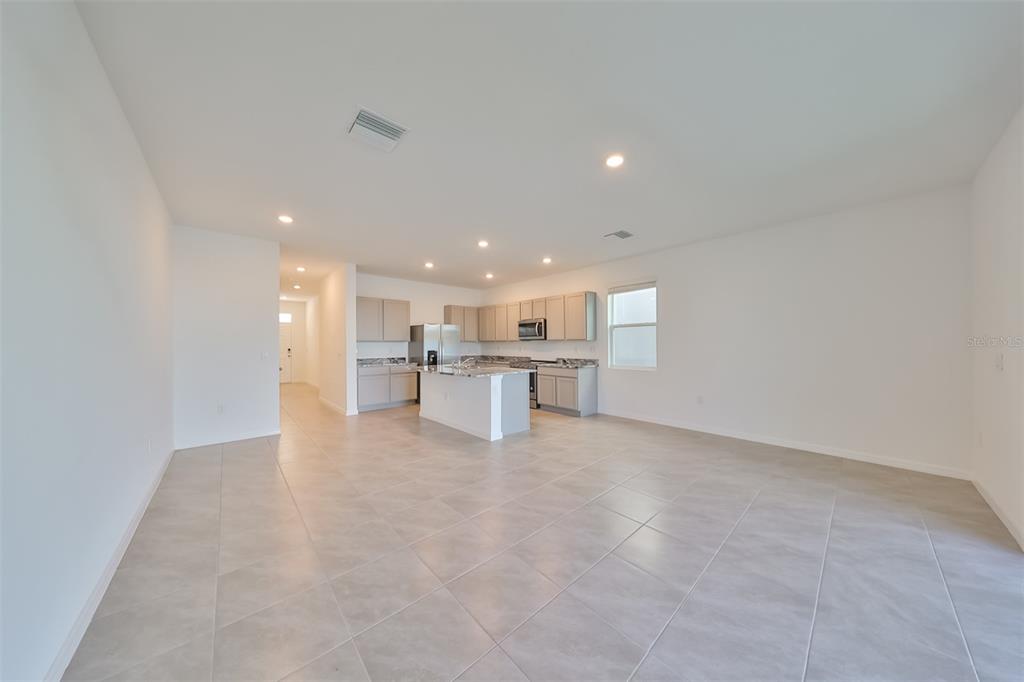 An open-concept kitchen with light-colored cabinets and a central island overlooks a tiled living area — 379 MANGROVE SHADE CIRCLE, APOLLO BEACH, FL